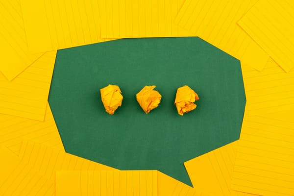 Three crumpled yellow papers on a green surface surrounded by yellow lined papers.